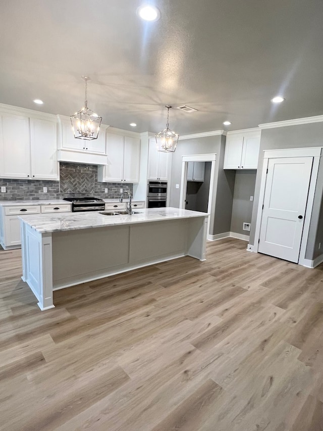 kitchen with decorative light fixtures, white cabinets, ornamental molding, a kitchen island with sink, and stainless steel appliances