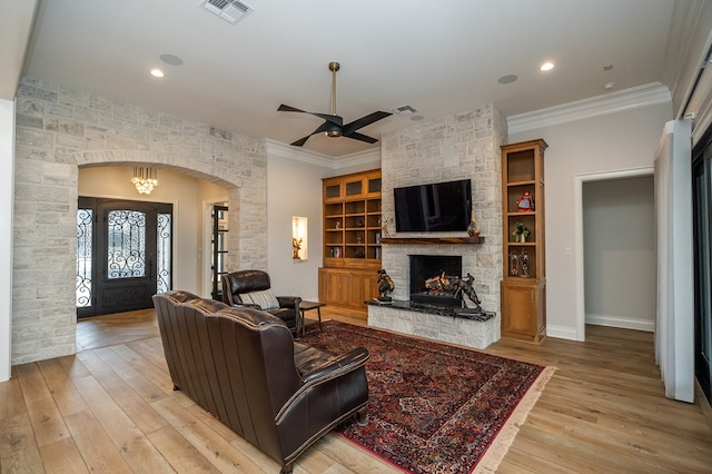 living room with a stone fireplace, ornamental molding, light hardwood / wood-style floors, and ceiling fan