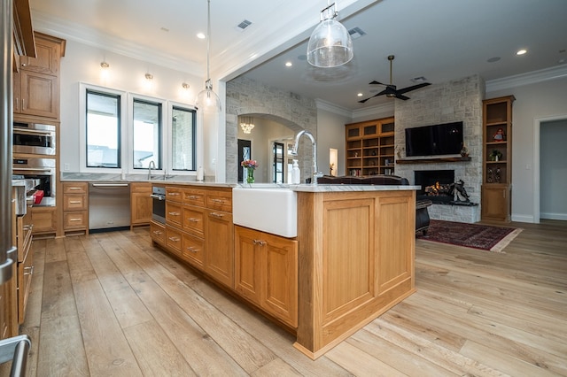 kitchen featuring an island with sink, stainless steel dishwasher, pendant lighting, and light hardwood / wood-style flooring