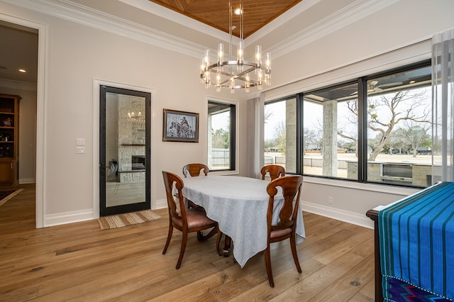 dining area with a raised ceiling, ornamental molding, an inviting chandelier, and light wood-type flooring