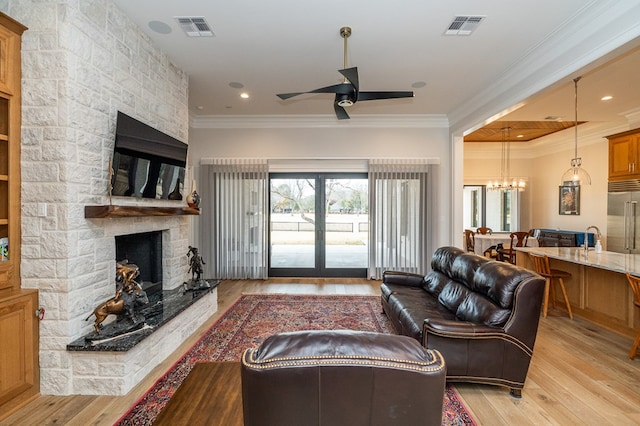 living room featuring crown molding, a fireplace, ceiling fan with notable chandelier, and light hardwood / wood-style floors