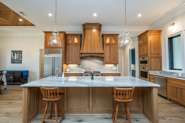 kitchen with a large island, a breakfast bar area, appliances with stainless steel finishes, decorative light fixtures, and custom exhaust hood