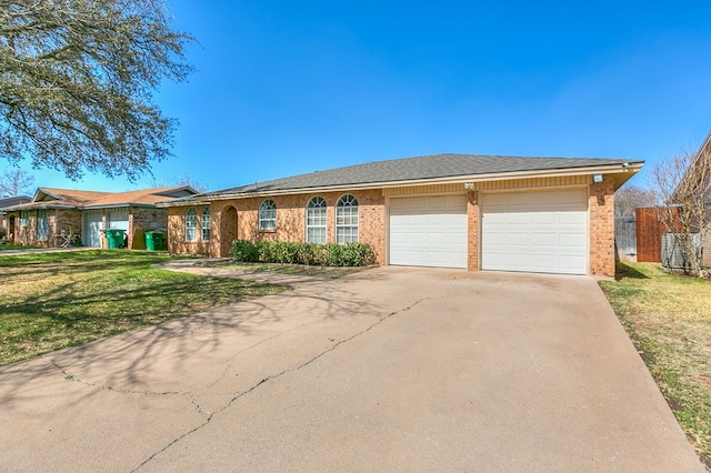 single story home featuring a front lawn, an attached garage, brick siding, and driveway