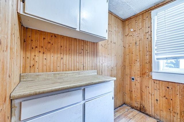 kitchen with white cabinetry, wooden walls, light hardwood / wood-style floors, and a textured ceiling