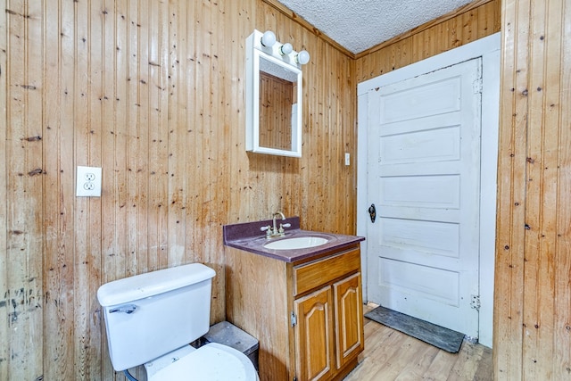 bathroom featuring wood walls, wood-type flooring, vanity, toilet, and a textured ceiling