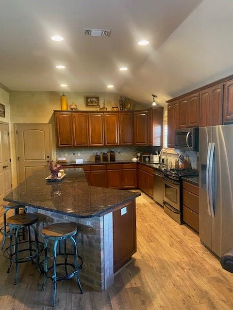 11725 Little Sorrel Trl, San Angelo, TX 76904 - kitchen featuring stainless steel appliances, light wood finished floors, a breakfast bar, dark stone countertops, and lofted ceiling