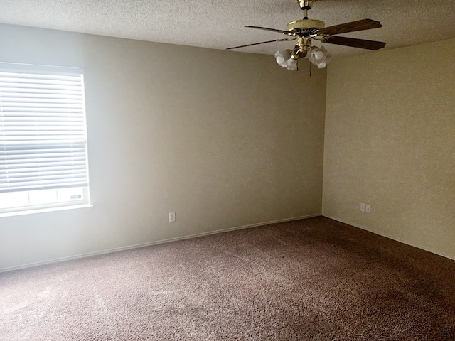 empty room with a ceiling fan, a healthy amount of sunlight, dark colored carpet, and a textured ceiling