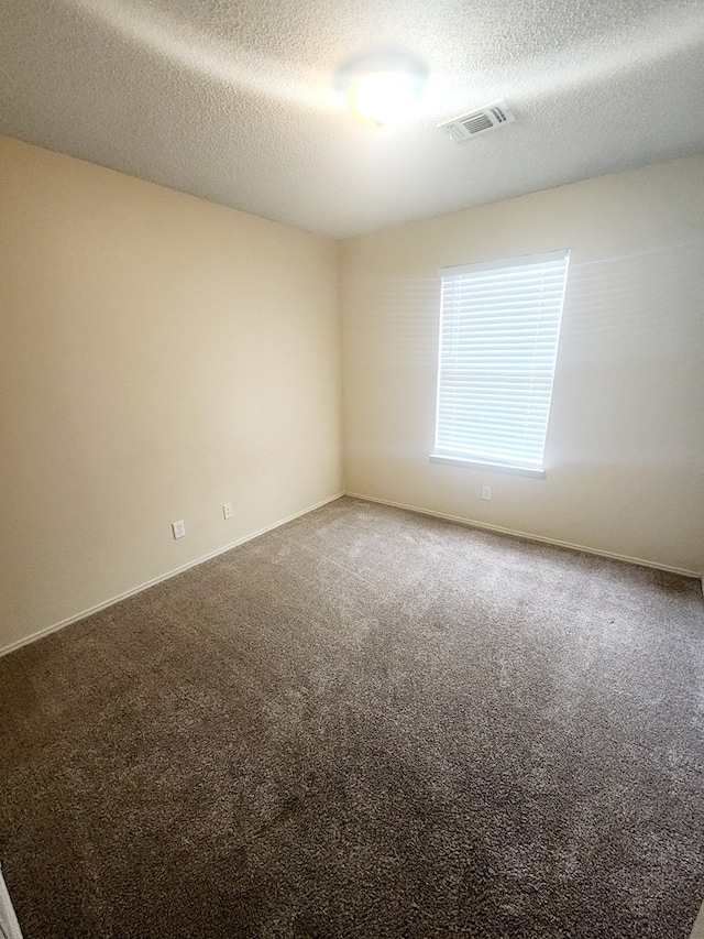 spare room with a textured ceiling, baseboards, visible vents, and carpet floors