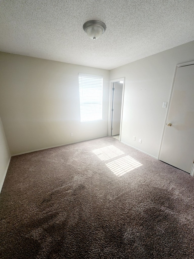 spare room with a textured ceiling, baseboards, and carpet