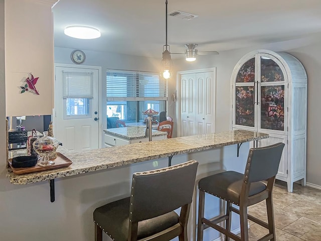 kitchen with light stone counters, decorative light fixtures, a kitchen breakfast bar, kitchen peninsula, and ceiling fan