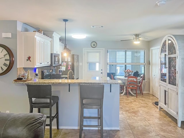 kitchen featuring decorative light fixtures, a breakfast bar, kitchen peninsula, and white cabinets