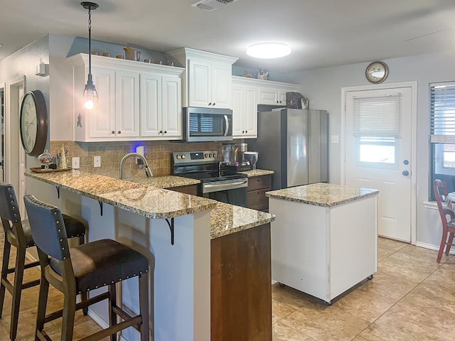 kitchen featuring white cabinetry, tasteful backsplash, light stone counters, hanging light fixtures, and appliances with stainless steel finishes