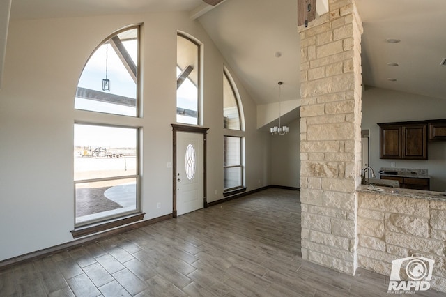 entrance foyer featuring a chandelier, high vaulted ceiling, wood finished floors, baseboards, and ornate columns