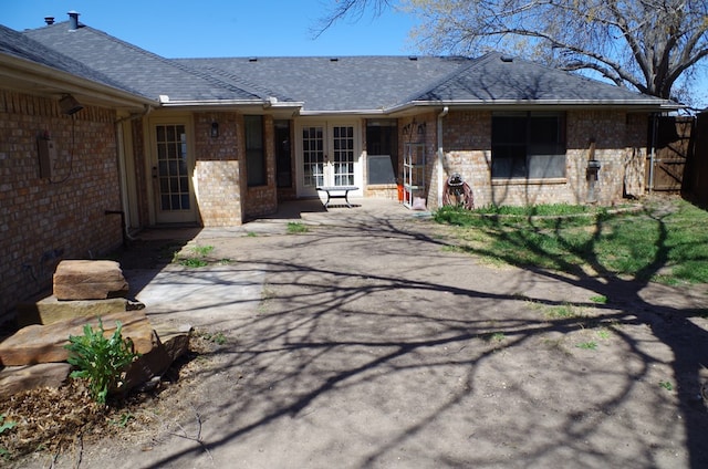 exterior space featuring french doors, a patio, brick siding, and roof with shingles