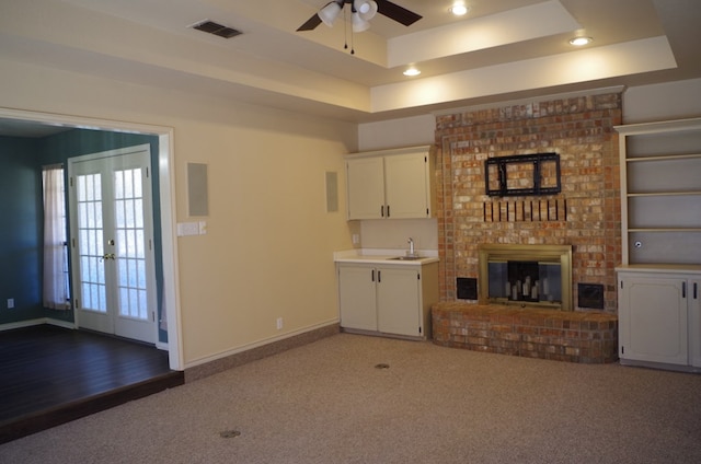 unfurnished living room with a ceiling fan, visible vents, baseboards, a tray ceiling, and a brick fireplace