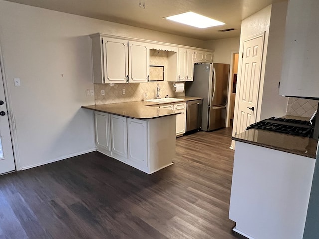 kitchen with appliances with stainless steel finishes, a peninsula, dark wood-style floors, white cabinets, and a sink