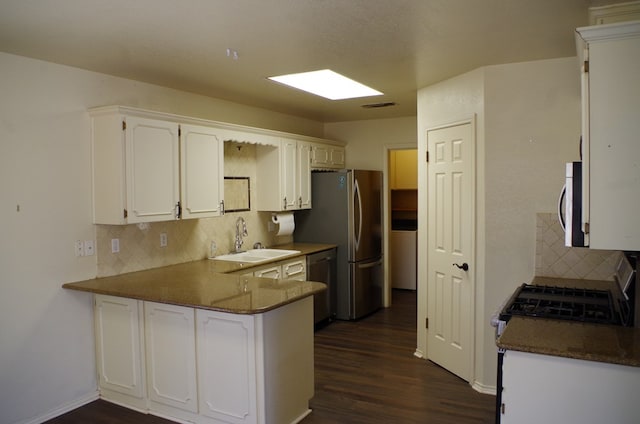 kitchen featuring visible vents, dark wood finished floors, a peninsula, stainless steel appliances, and a sink