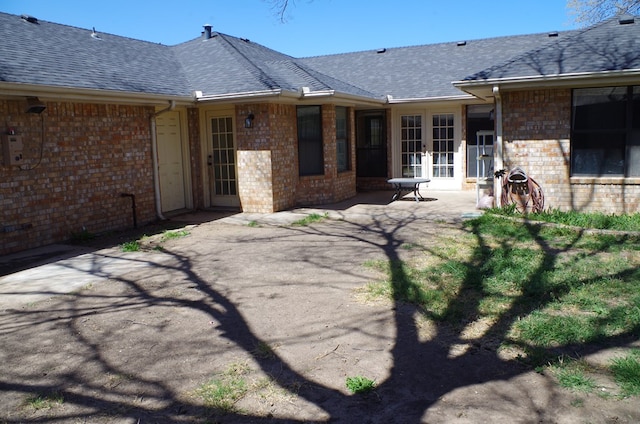 rear view of property with a patio area, french doors, brick siding, and a shingled roof