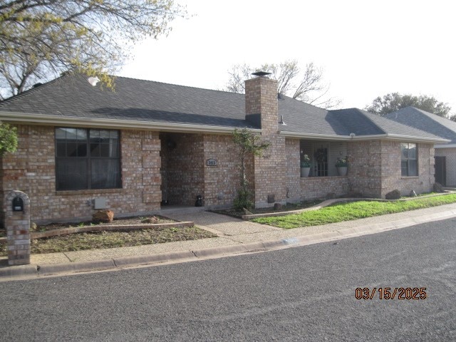 single story home with brick siding, a chimney, and a shingled roof