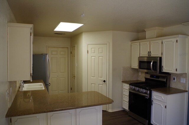 kitchen with backsplash, appliances with stainless steel finishes, a peninsula, white cabinetry, and a sink