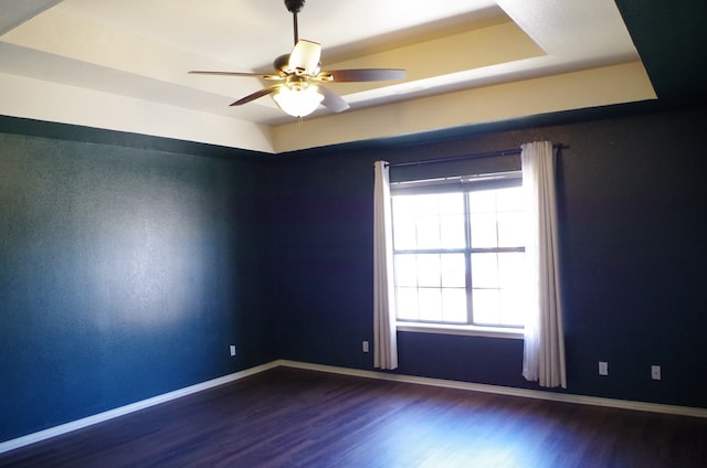 empty room featuring baseboards, a raised ceiling, wood finished floors, and a ceiling fan