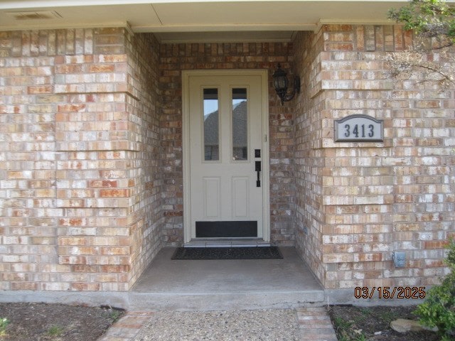 doorway to property with visible vents, stone siding, and brick siding