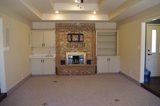 unfurnished living room featuring a sink, a tray ceiling, light carpet, and baseboards