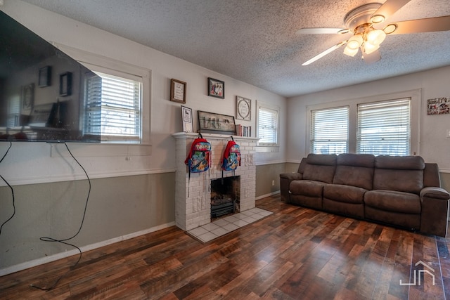 living room featuring dark hardwood / wood-style flooring, a brick fireplace, a textured ceiling, and ceiling fan