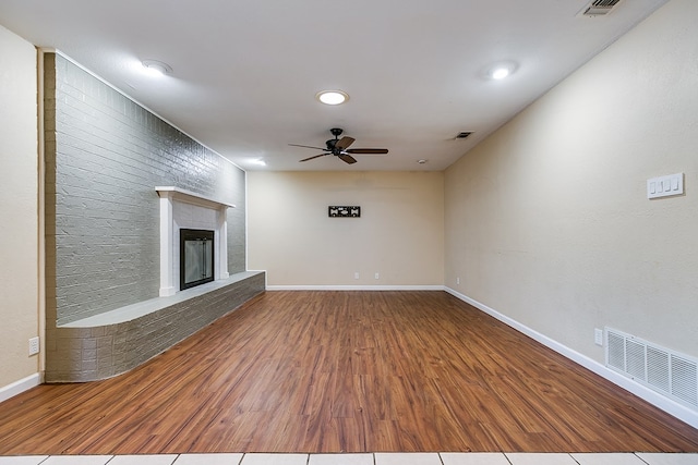 unfurnished living room featuring ceiling fan, wood-type flooring, and a brick fireplace