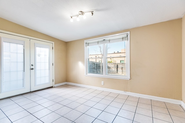 tiled empty room featuring vaulted ceiling, a healthy amount of sunlight, a textured ceiling, and french doors