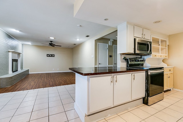 kitchen with white cabinetry, light tile patterned floors, appliances with stainless steel finishes, ceiling fan, and a fireplace