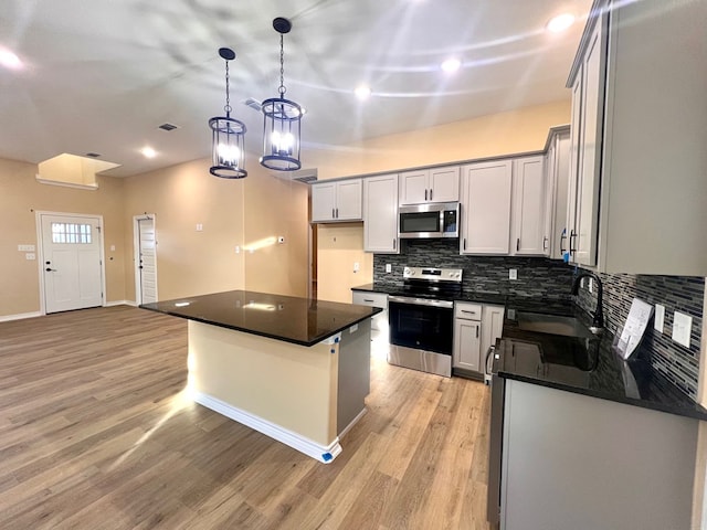 kitchen with dark countertops, light wood finished floors, decorative backsplash, appliances with stainless steel finishes, and a sink