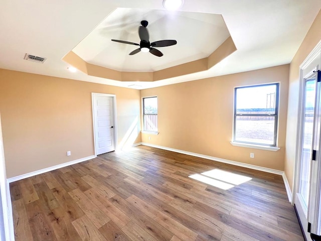 spare room featuring visible vents, a ceiling fan, a tray ceiling, wood finished floors, and baseboards