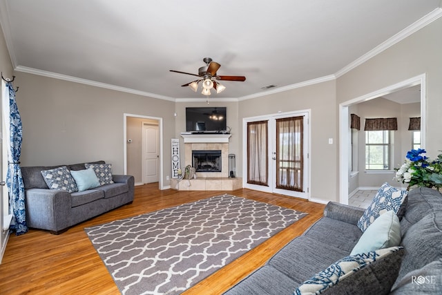 living room featuring hardwood / wood-style flooring, ceiling fan, ornamental molding, and a tile fireplace