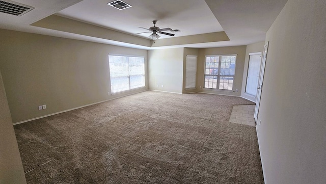 carpeted spare room featuring ceiling fan and a raised ceiling