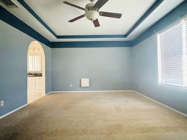 interior space featuring a raised ceiling, connected bathroom, light colored carpet, and ceiling fan