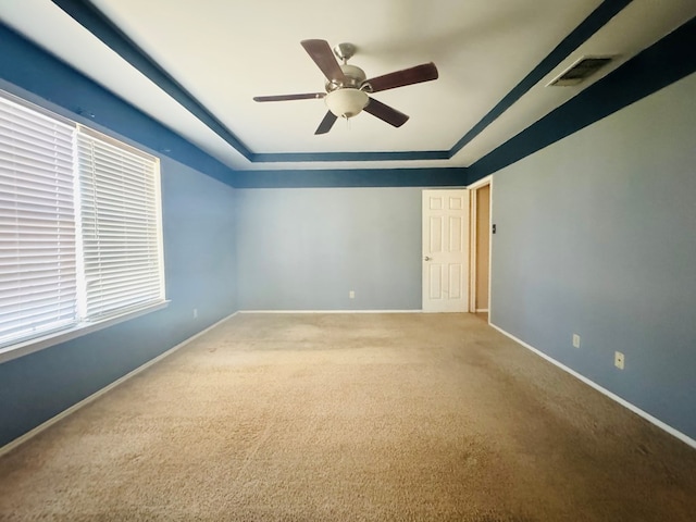 carpeted empty room featuring a raised ceiling and ceiling fan