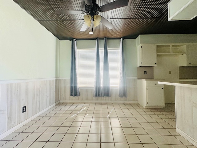 kitchen featuring light tile patterned floors, wood ceiling, ceiling fan, white cabinets, and wood walls