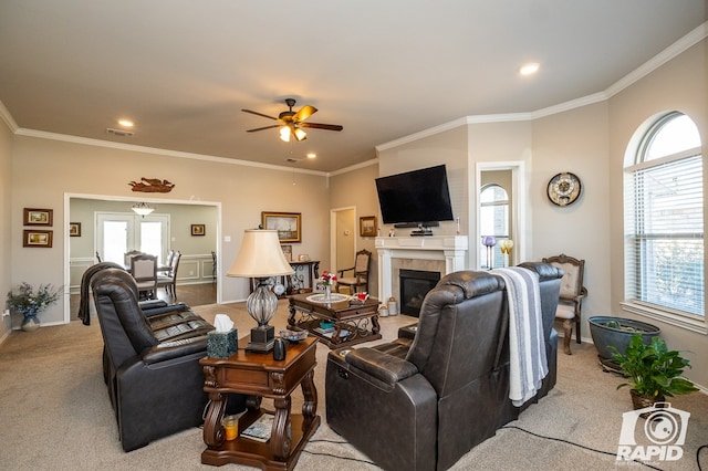 living room with a tiled fireplace, ornamental molding, light carpet, and ceiling fan