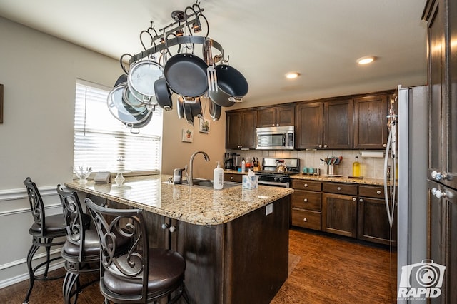 kitchen featuring sink, light stone counters, a kitchen breakfast bar, stainless steel appliances, and backsplash