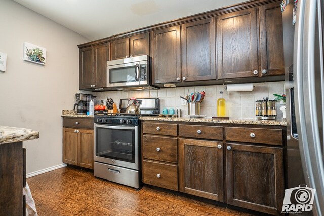 kitchen featuring light stone counters, appliances with stainless steel finishes, dark wood-style flooring, dark brown cabinets, and backsplash