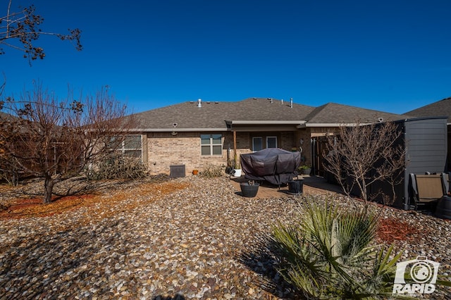 back of property with central air condition unit, roof with shingles, a patio, and brick siding