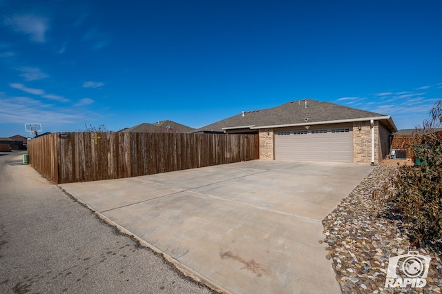 exterior space featuring brick siding, a shingled roof, concrete driveway, fence, and a garage