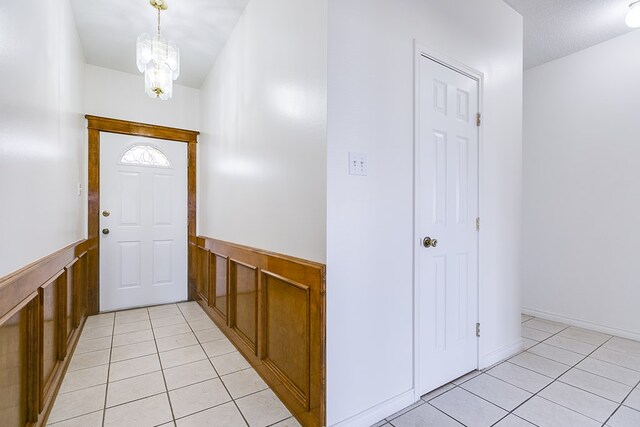 foyer with a notable chandelier, light tile patterned floors, and a wainscoted wall