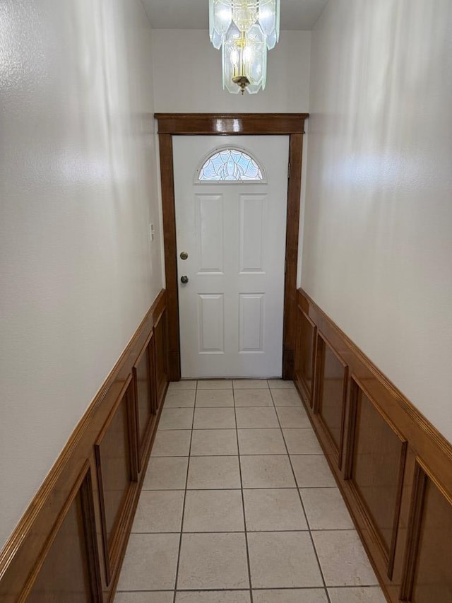 doorway to outside with light tile patterned floors, a notable chandelier, and wainscoting