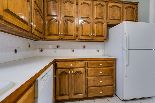 kitchen with backsplash, white appliances, light tile patterned flooring, brown cabinetry, and light countertops