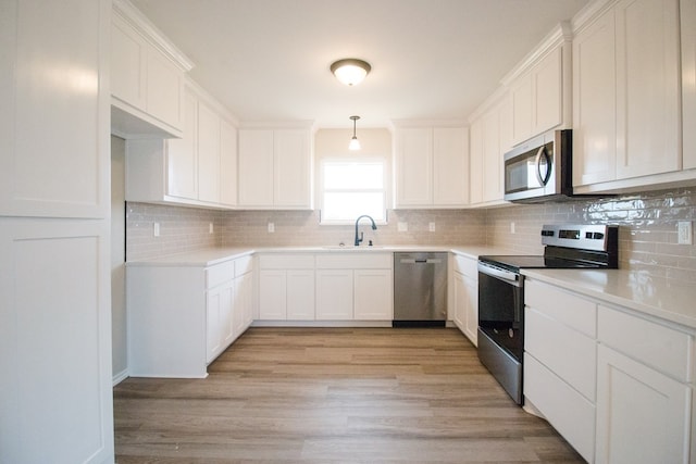 kitchen featuring sink, white cabinetry, hanging light fixtures, light wood-type flooring, and stainless steel appliances