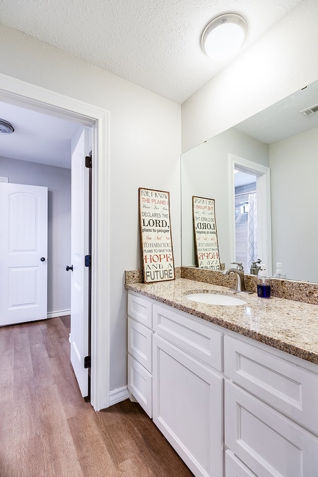 bathroom with a textured ceiling, wood finished floors, vanity, visible vents, and baseboards