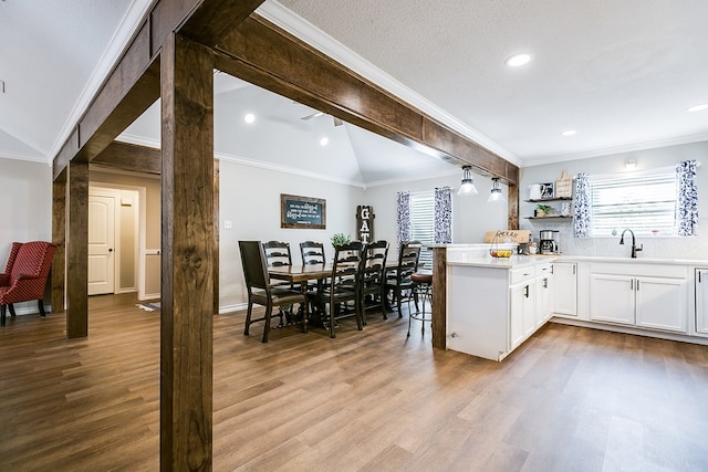 kitchen with lofted ceiling with beams, ornamental molding, white cabinets, wood finished floors, and a peninsula