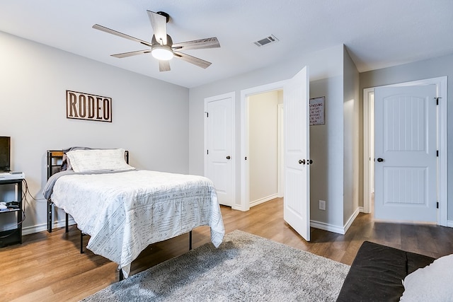 bedroom with a ceiling fan, visible vents, baseboards, and wood finished floors